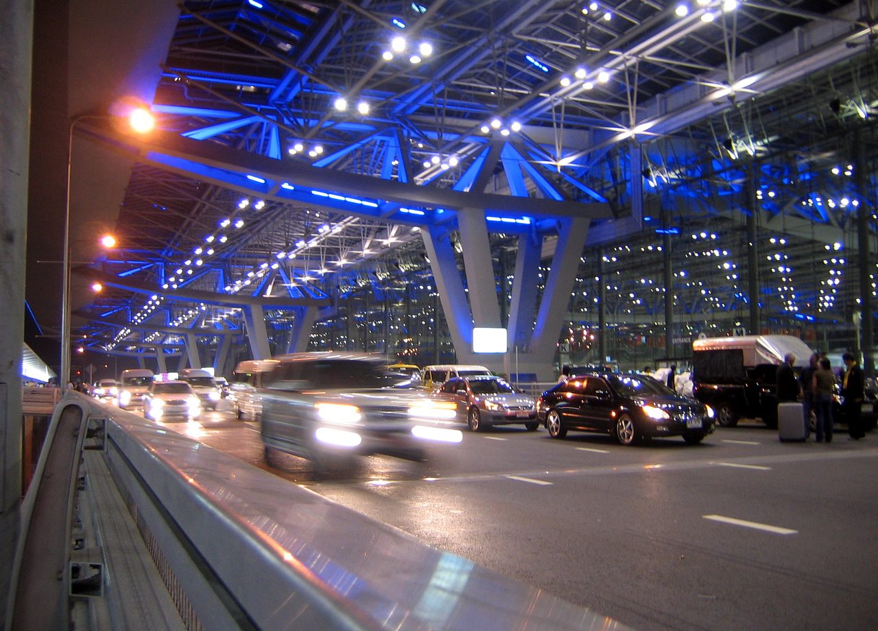 Vehicles waiting curbside under a lit airport terminal canopy at night