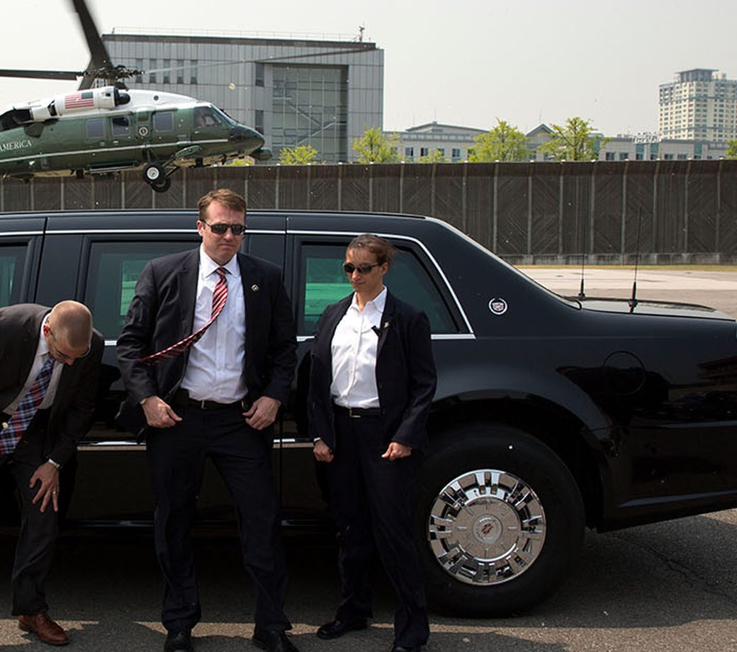 Drivers in business suits standing at the door of a black executive vehicle