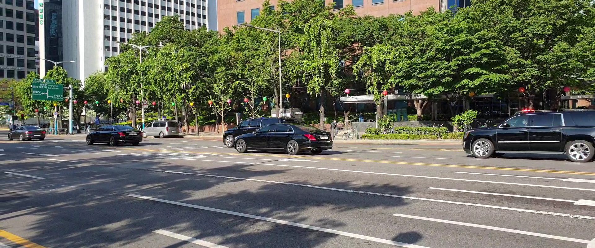 A line of black executive vehicles running along a city boulevard