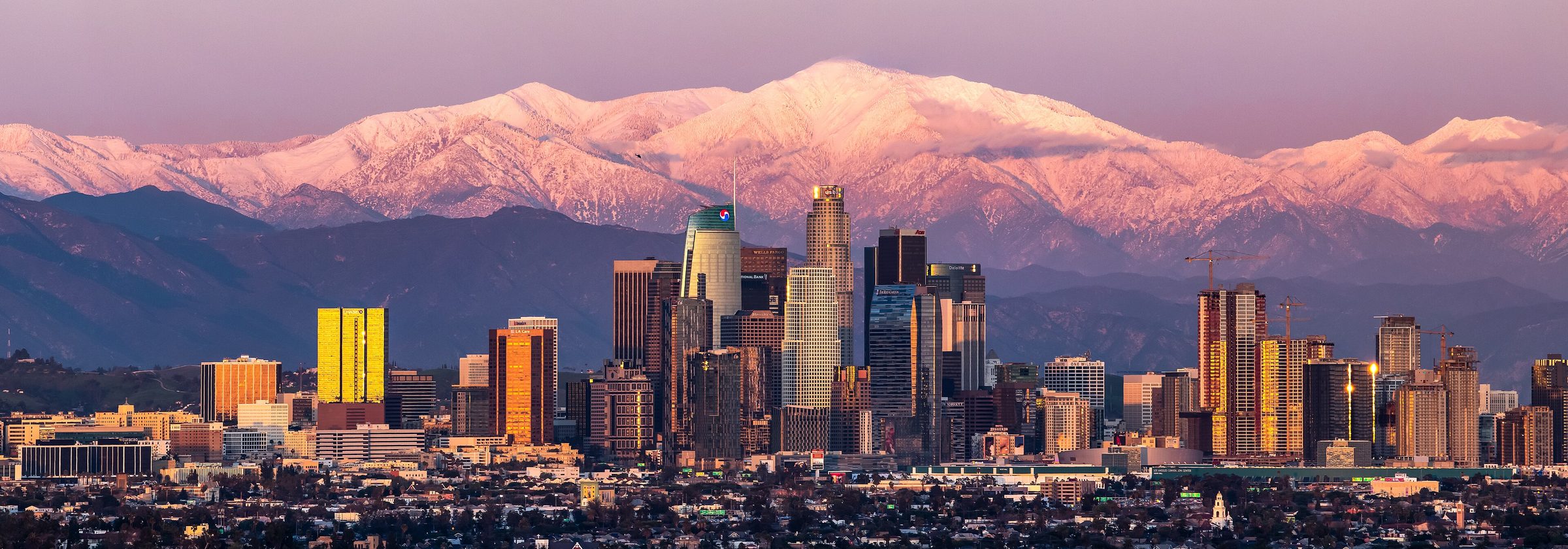 Downtown Los Angeles skyline at sunset with the snow-capped San Gabriel Mountains behind